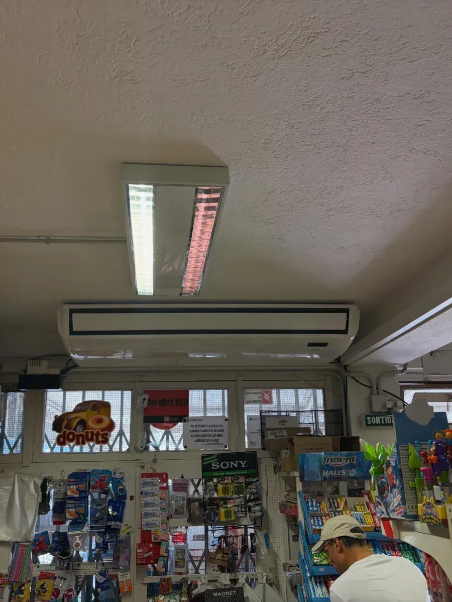 Interior de una tienda de conveniencia, con luces fluorescentes, estantes de snacks y un cajero cerca del mostrador