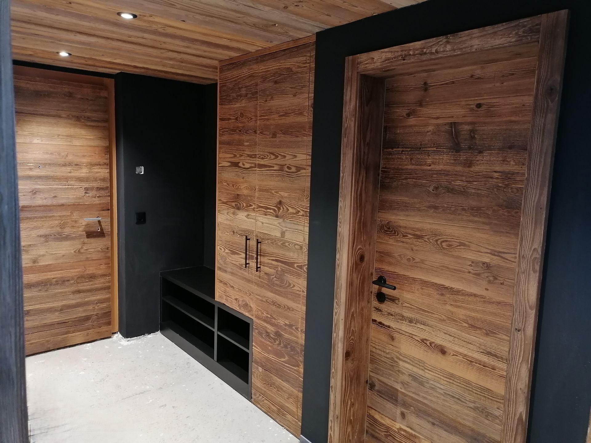 Ein Raum mit einer Holzwand und einem weissen Holzschrank. Foto von der Holzprofi Zermatt AG