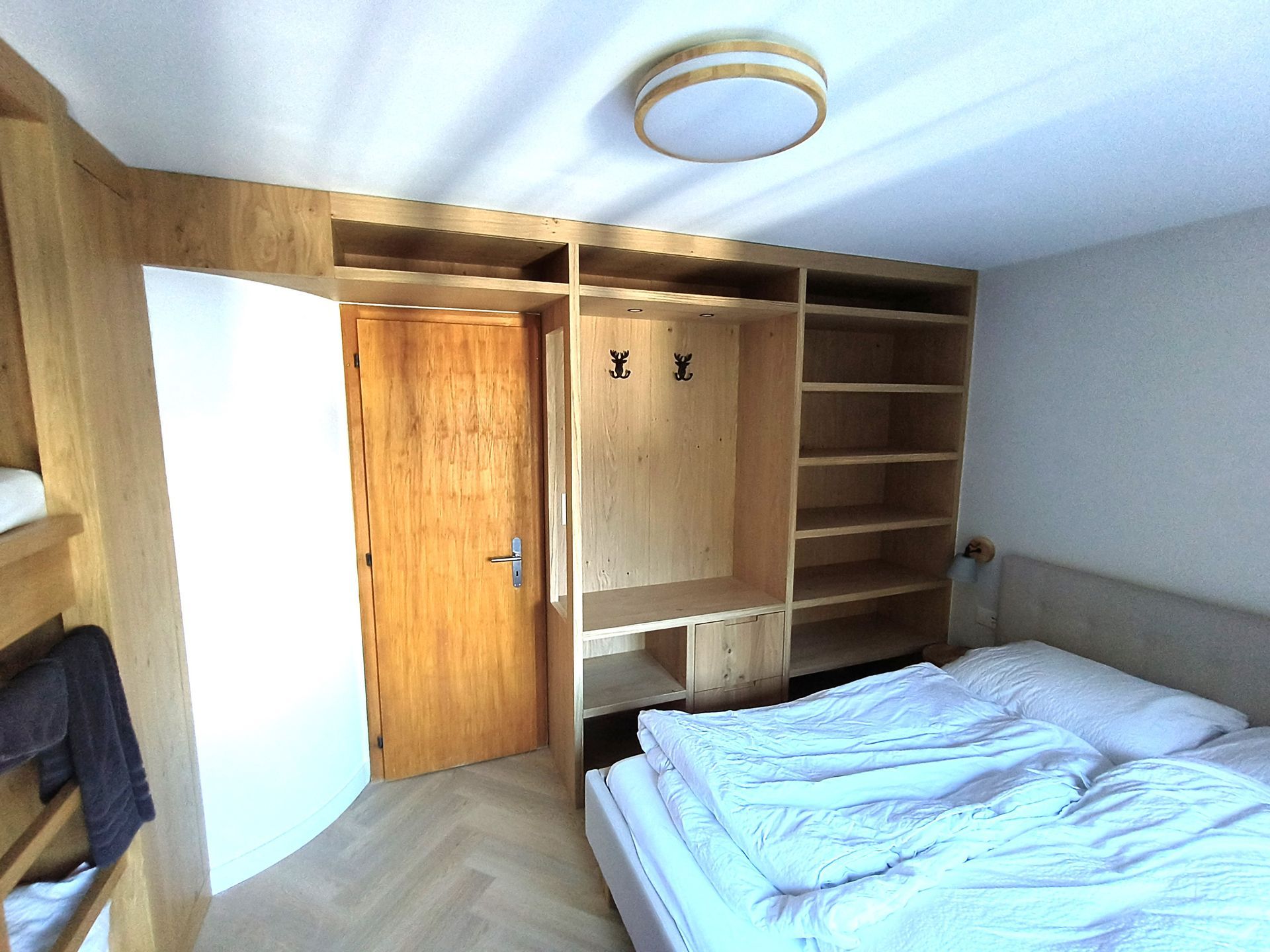 Ein Schlafzimmer mit einem Bett und an der Wand hängender Kleidung auf Holzrahmen. Foto von der Holzprofi Zermatt AG