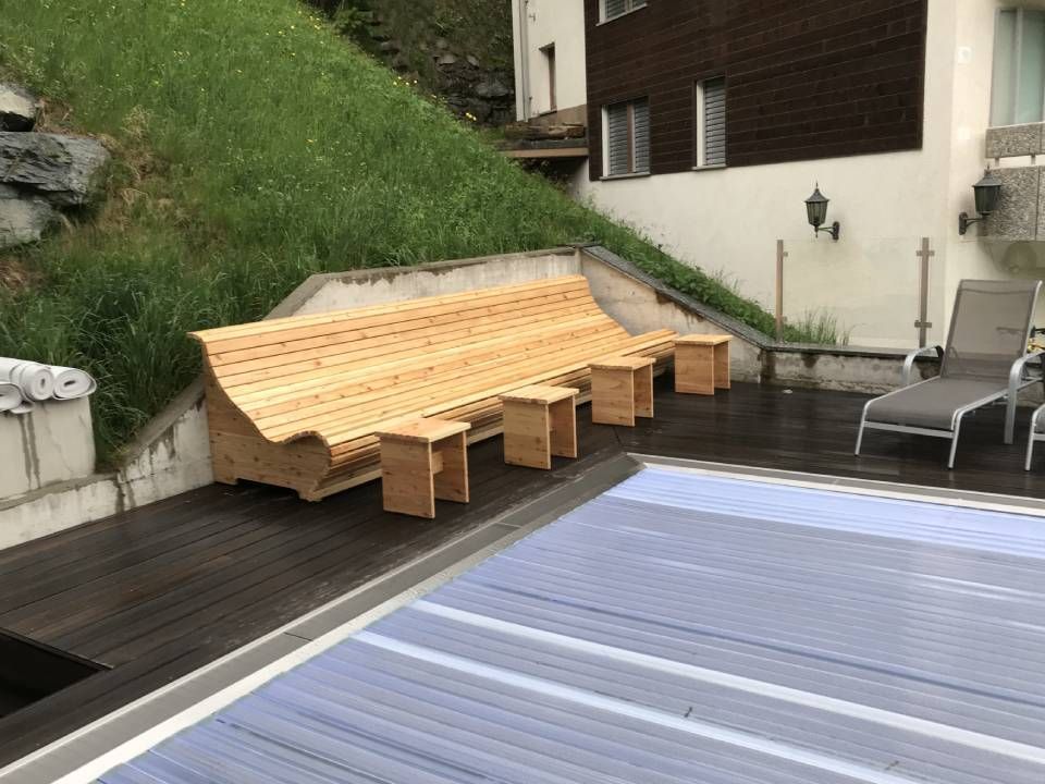 Neben einem Swimmingpool steht eine Holzbank. Foto von der Holzprofi Zermatt AG