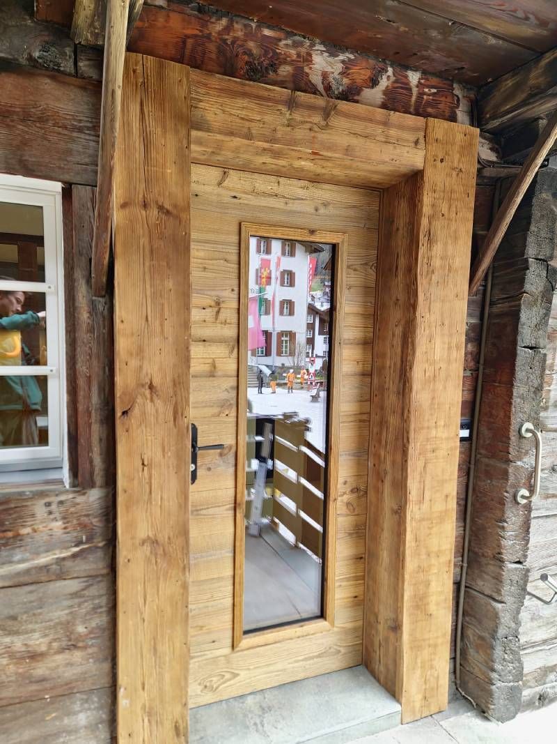 Eine Holztür mit einem Glasfenster in einem Holzgebäude. Foto von der Holzprofi Zermatt AG