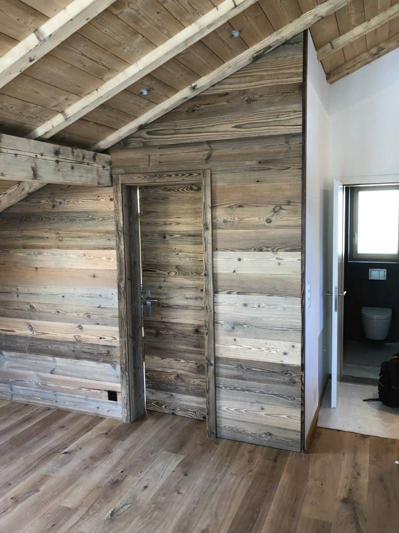 Ein Raum mit Holzwänden und einer Tür, die zu einem Badezimmer führt. Foto von der Holzprofi Zermatt AG