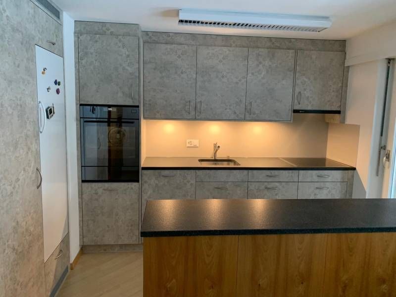 Eine Küche mit grauen Schränken, schwarzen Arbeitsplatten, einer Spüle und einem Ofen.  Foto von der Holzprofi Zermatt AG