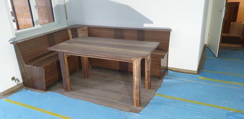 Ein Holztisch und eine Bank in einem Raum mit blauem Boden.  Foto von der Holzprofi Zermatt AG