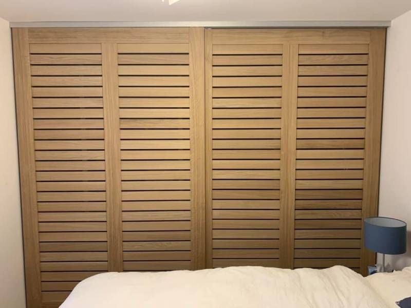 Ein Schlafzimmer mit einem Bett und hölzernen Fensterläden an der Wand.  Foto von der Holzprofi Zermatt AG