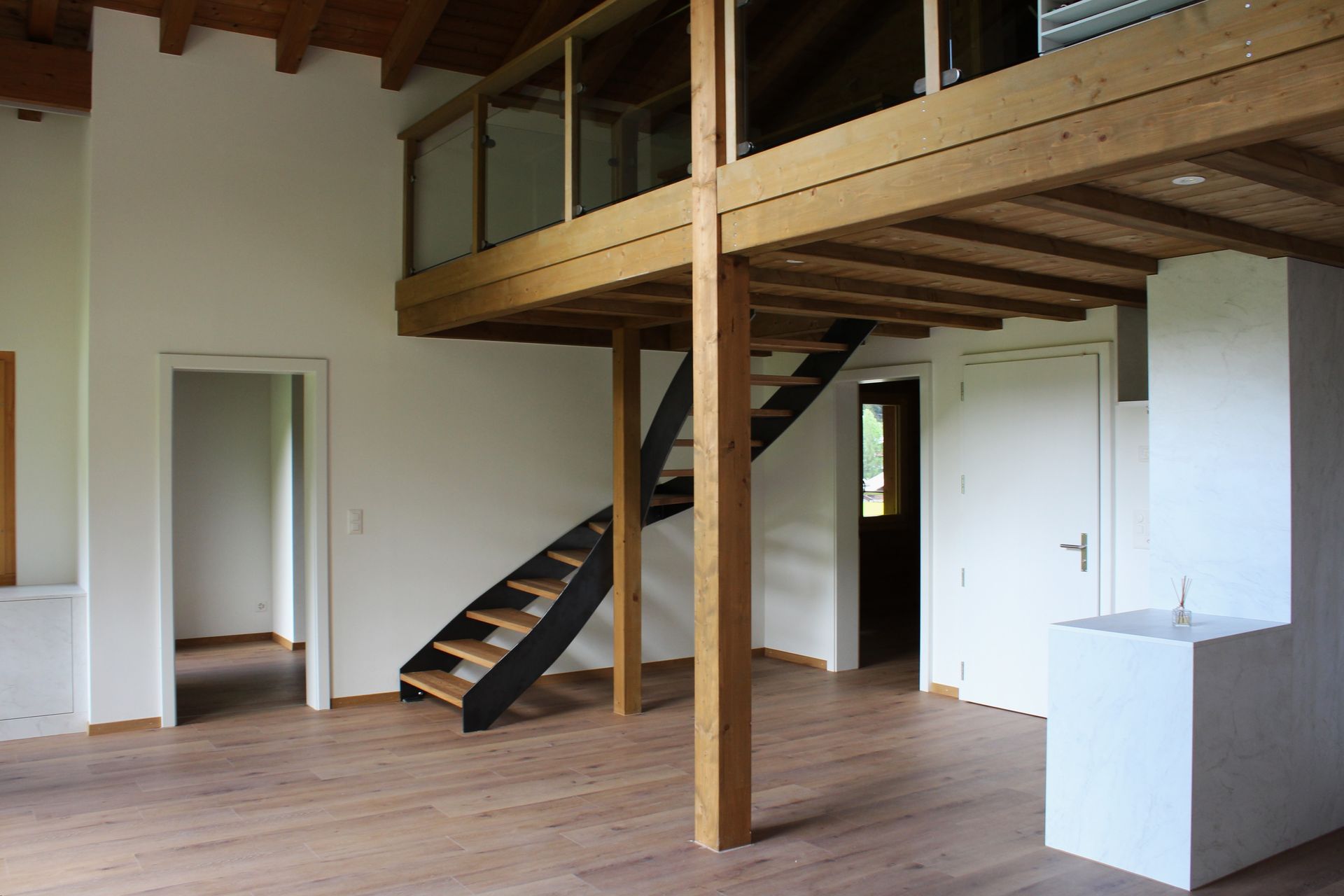 Vor einem Gebäude steht ein Holzhaus mit Balkon und Treppe. Foto von der Holzprofi Zermatt AG