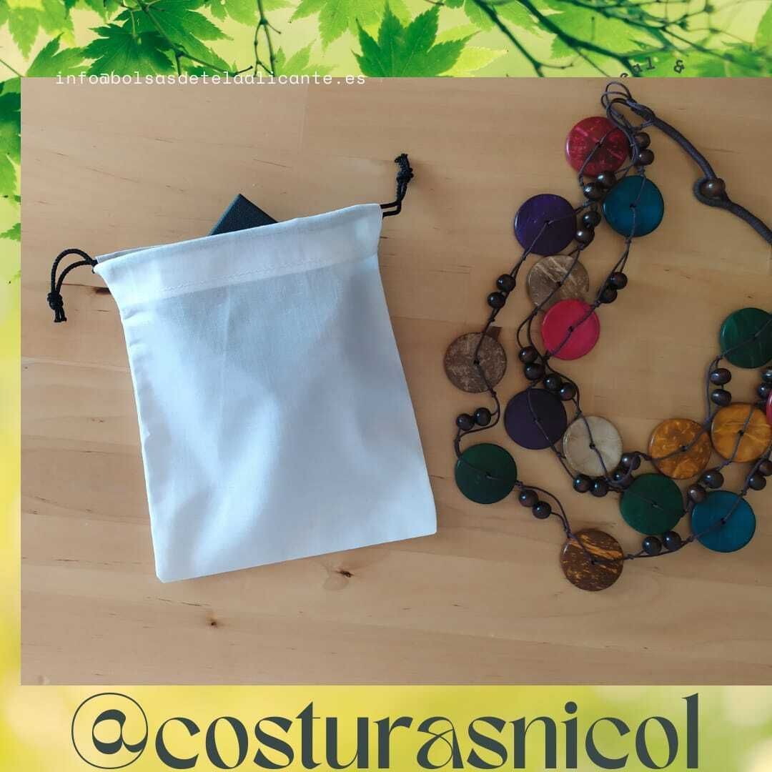 Un collar colorido se encuentra sobre una mesa de madera junto a una bolsa blanca.