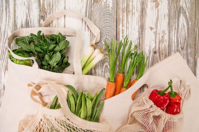 Tres bolsas llenas de verduras están sobre una mesa de madera.