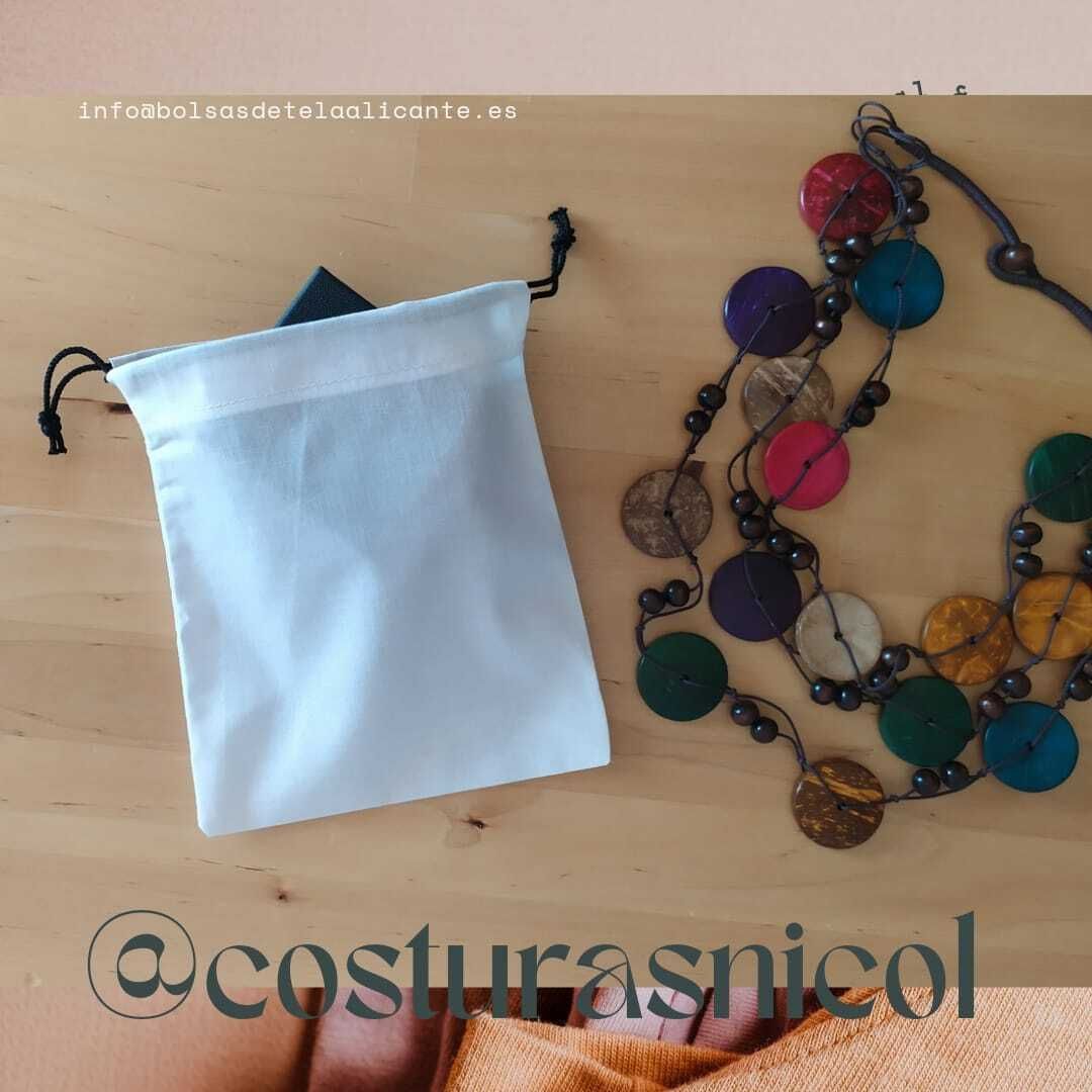 Un collar está sobre una mesa al lado de una bolsa blanca que dice costurasnicol