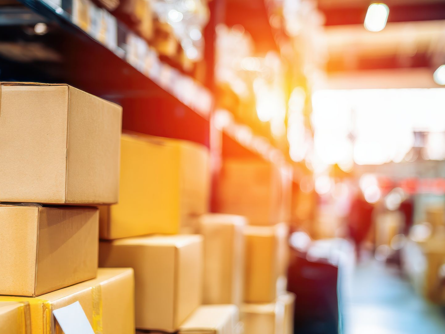 Des cartons empilés sur des étagères dans un entrepôt, sous une lumière vive.