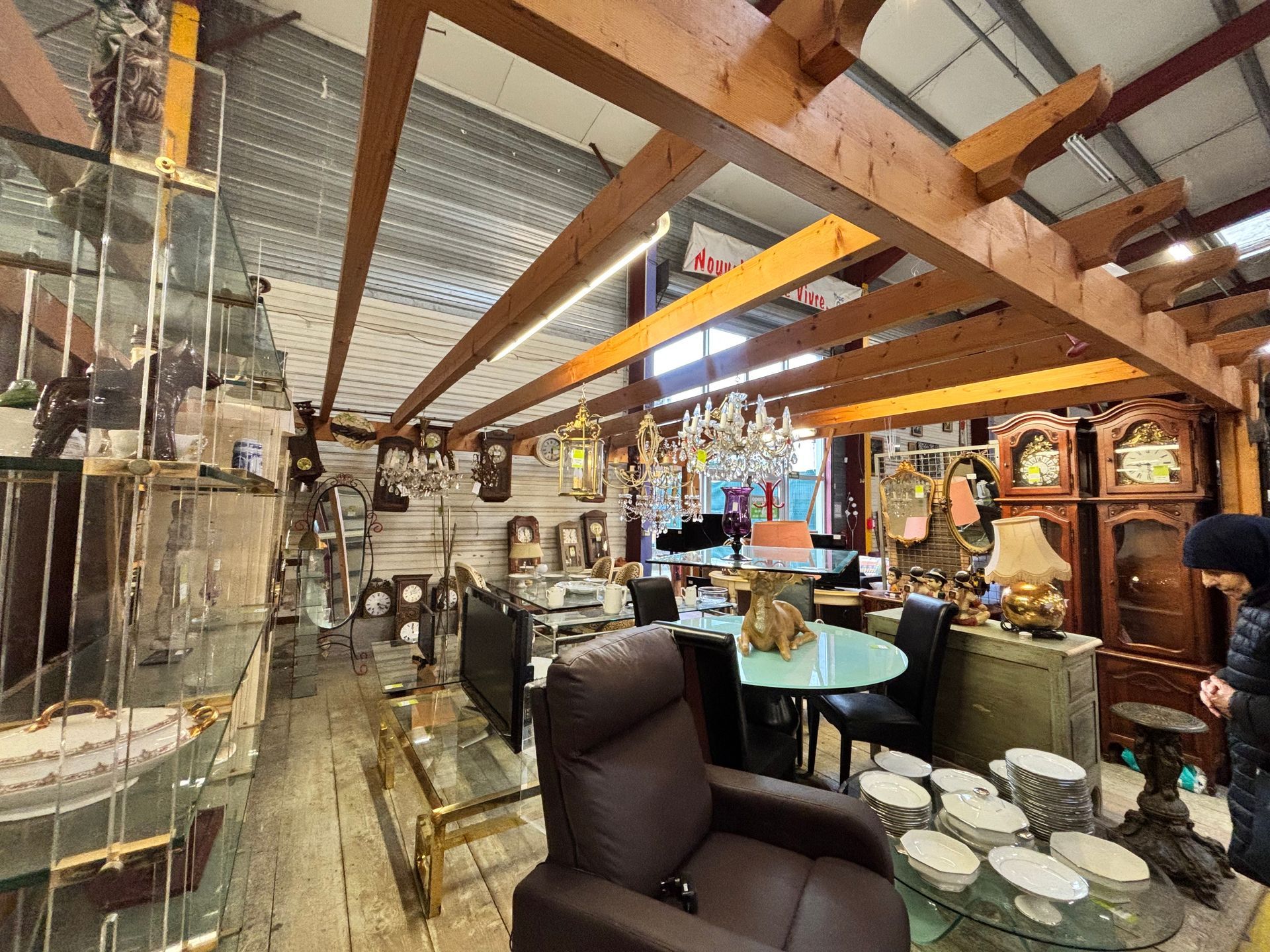 Intérieur d'un magasin d'antiquités avec meubles, horloges et objets de décoration sous des poutres apparentes.