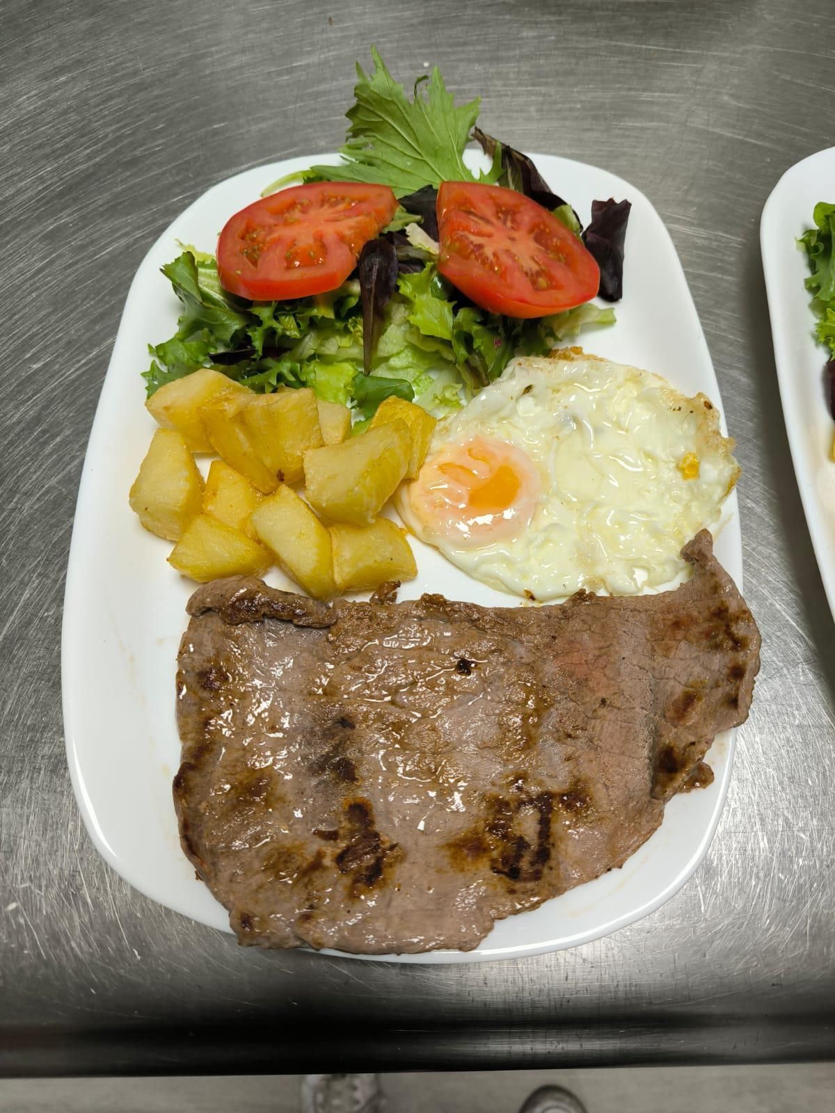 Bistec, huevo frito, patatas y ensalada en un plato blanco.