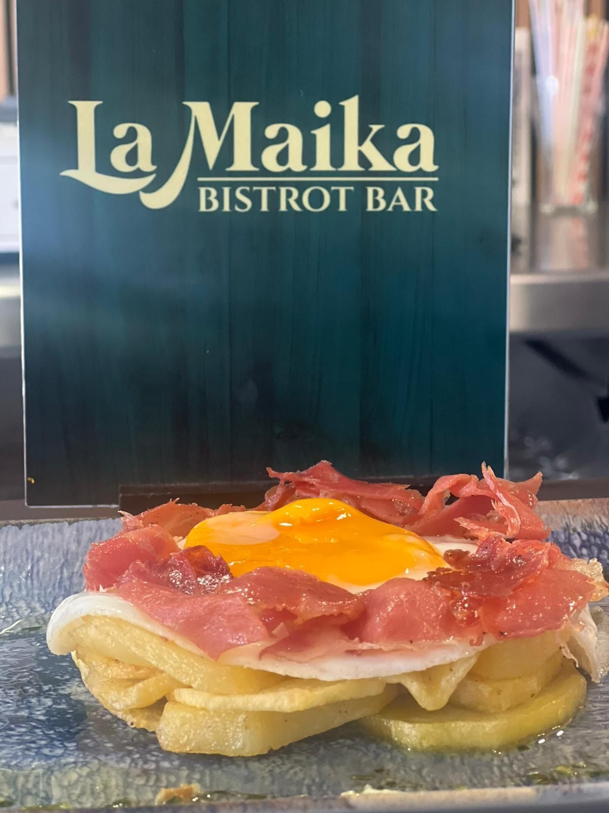 Plato con huevo frito, patatas y jamón, frente al cartel del bar bistro 