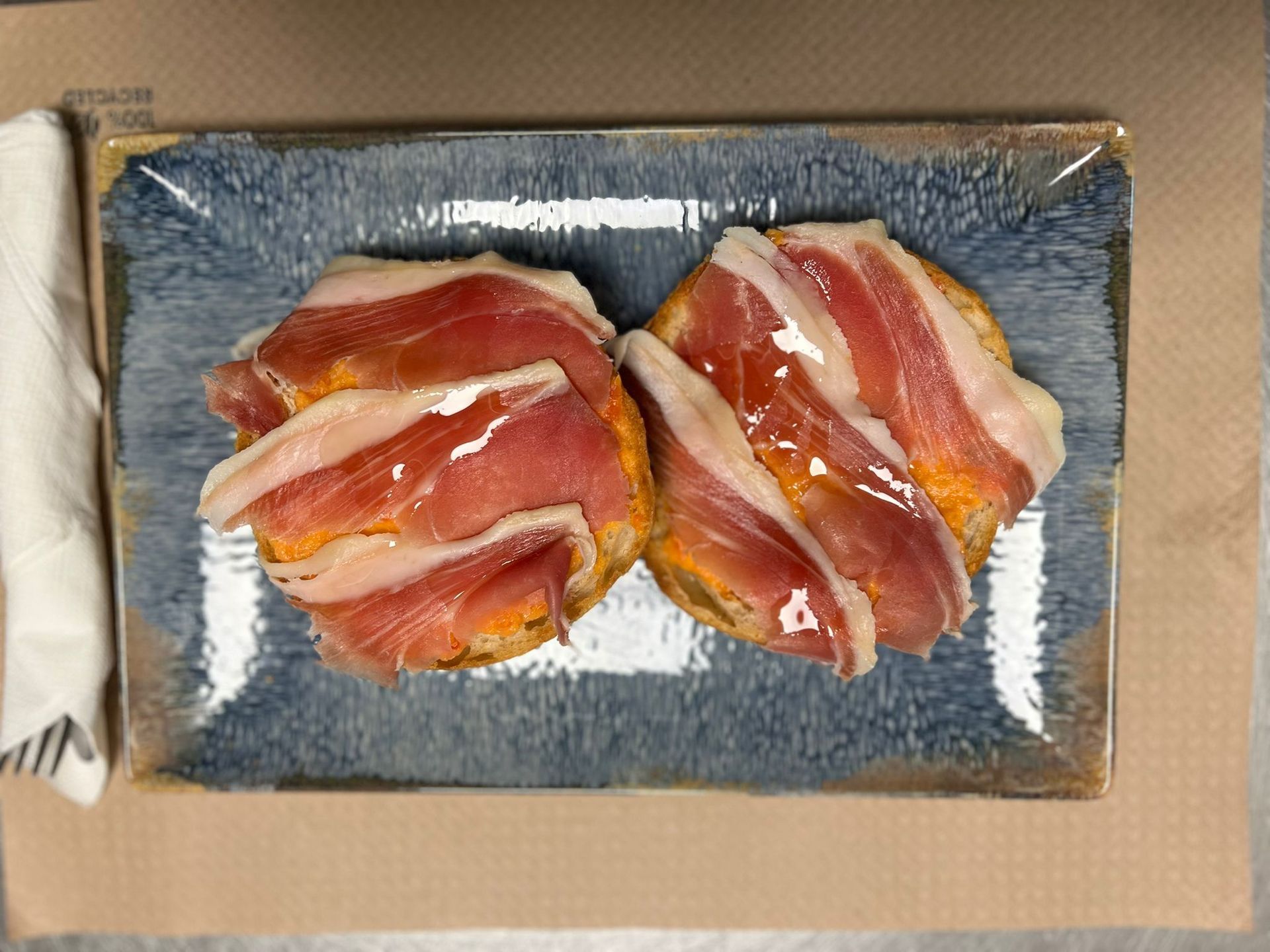 Dos rebanadas de pan tostado cubiertas con finas lonchas de jamón, sobre un plato rectangular azul.