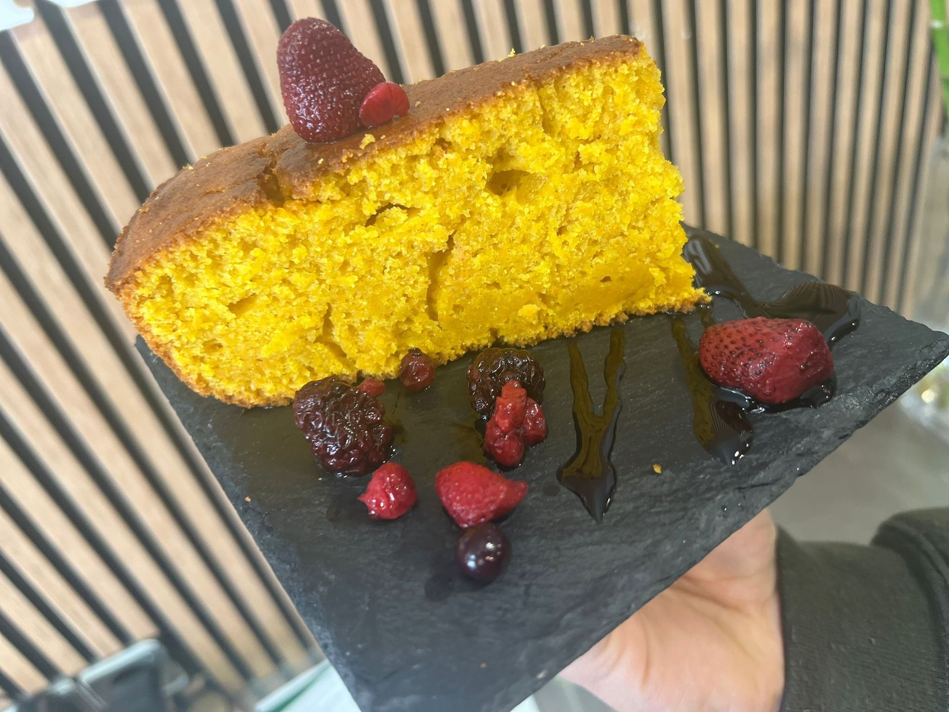 Rebanada de pastel de naranja adornada con bayas, servida en un plato cuadrado negro.
