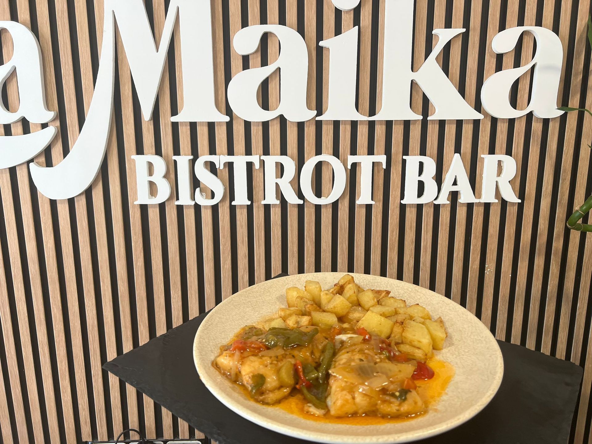 Plato de comida con patatas y pescado delante del cartel de un restaurante, 