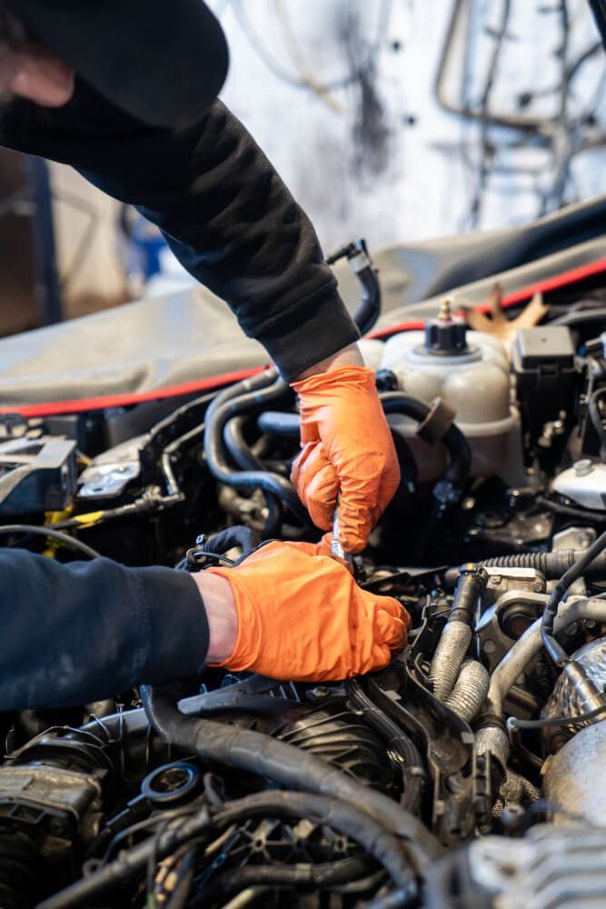 A man wearing orange gloves is working on a car engine.