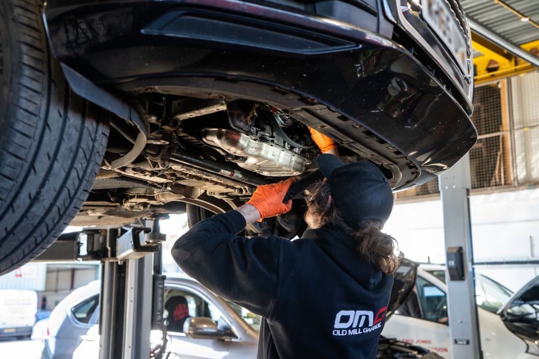 A man is working on the underside of a car in a garage.