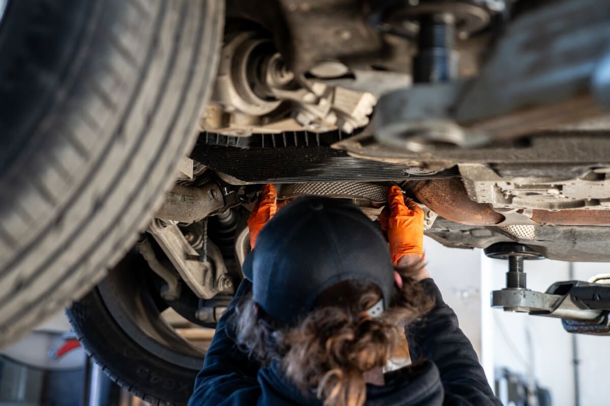 A woman is working under a car in a garage.