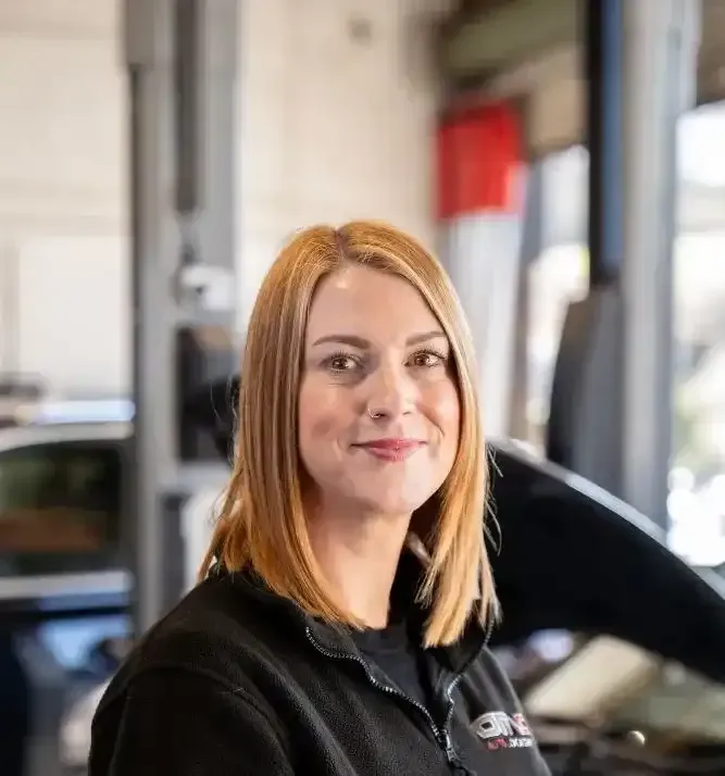 A woman is standing in front of a car in a garage.