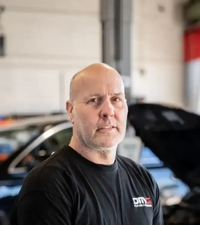 A man in a black shirt is standing in front of a car with the hood up.