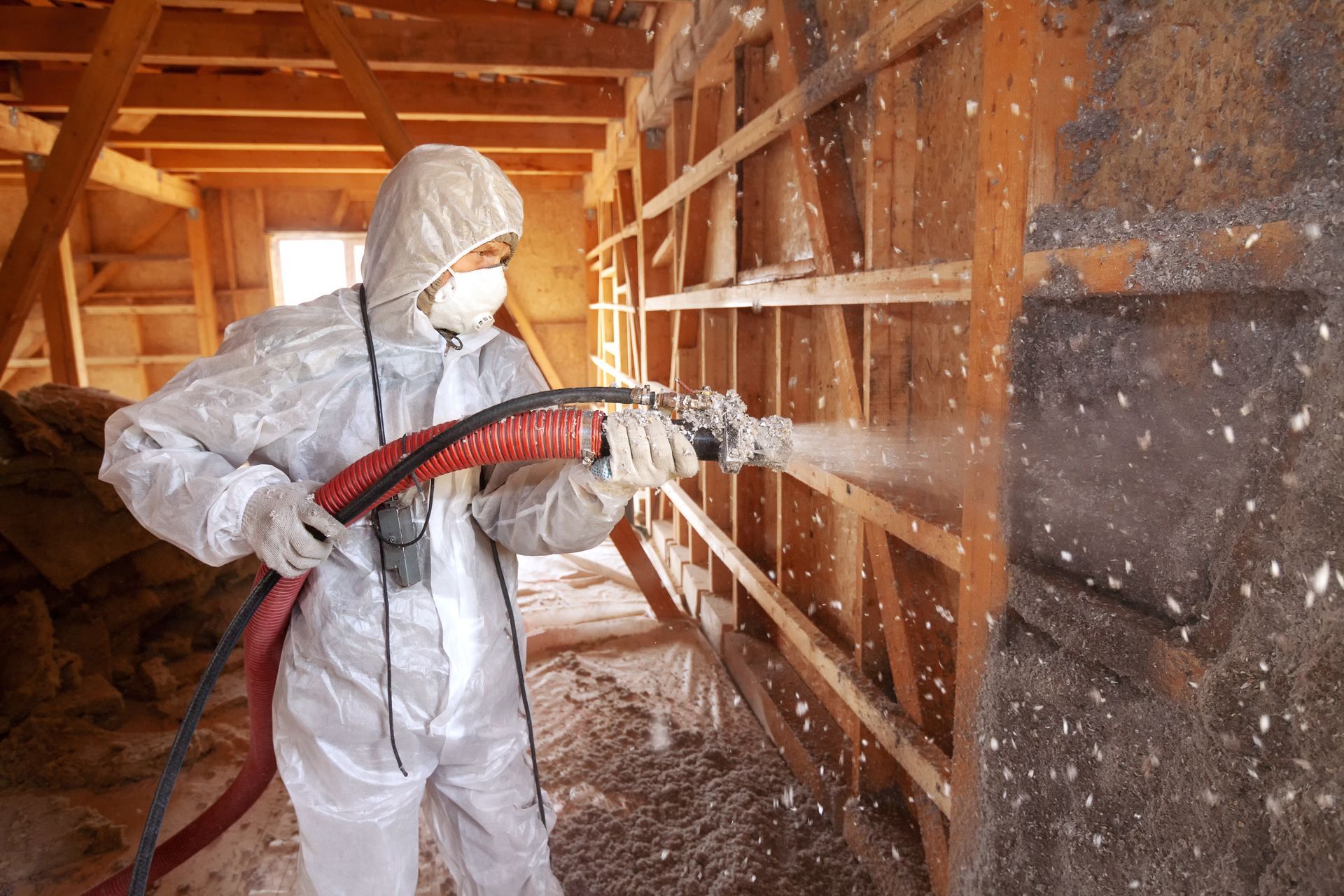 Un homme utilise une lance pour projeter de la laine de roche dans les murs d'une maison