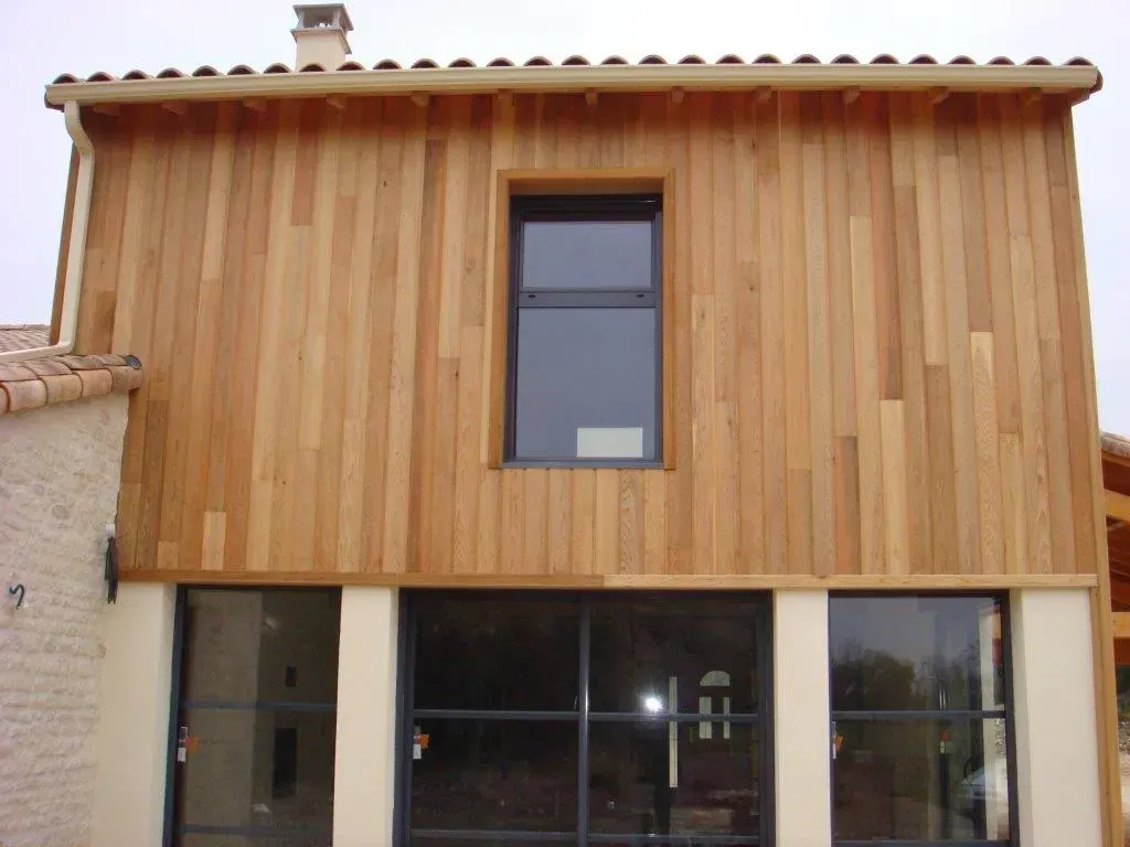 Une maison avec une baie vitrée au rez-de-chaussée et un bardage en bois au premier étage