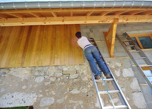 Une personne installe un bardage en bois sur une façade en parpaings