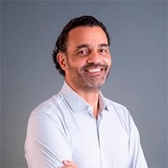 Um homem com barba está sorrindo para a câmera com os braços cruzados.