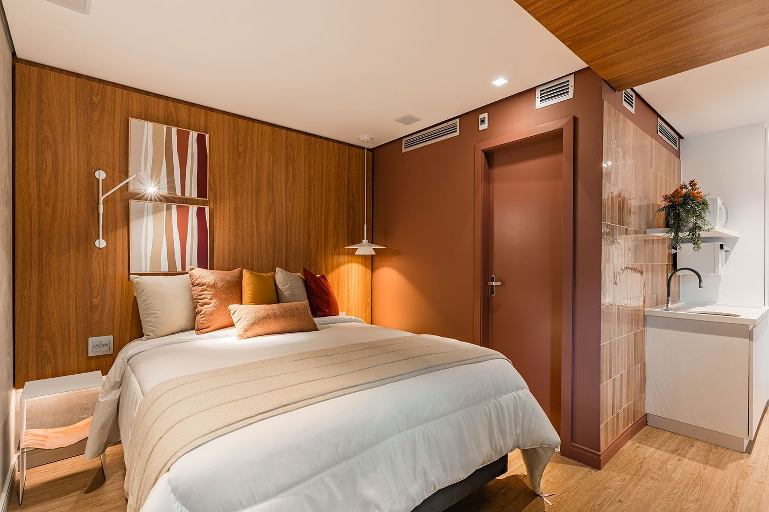 Quarto aconchegante com painéis de madeira, cama com roupa de cama branca e travesseiros coloridos e uma porta aberta.
