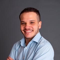 Um homem de camisa azul está sorrindo com os braços cruzados.