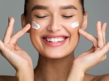 Una mujer sonríe mientras se aplica crema en la cara.