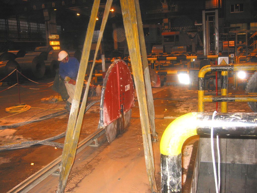 Obrero en una planta industrial junto a maquinaria roja y tuberías amarillas por la noche.