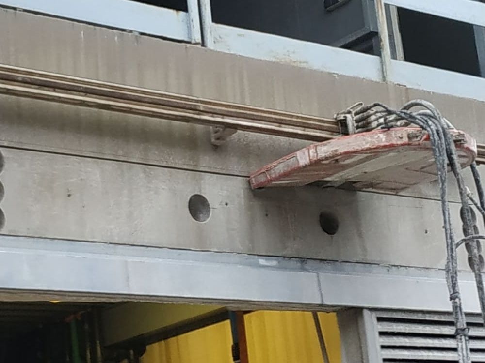 Obrero de la construcción en un elevador reparando la fachada de hormigón de un edificio cerca de las ventanas.