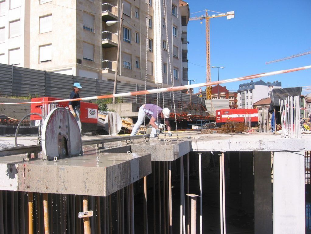 Obreros de la construcción en una plataforma de concreto en una obra, con una grúa y una cimentación sin terminar debajo.