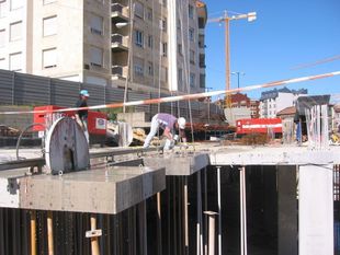 Obreros de la construcción sobre una losa de hormigón en una obra, con una grúa y estructuras sin terminar al fondo.
