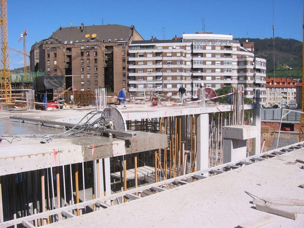Obra en construcción con estructuras de hormigón y bloques de apartamentos bajo un cielo azul despejado.