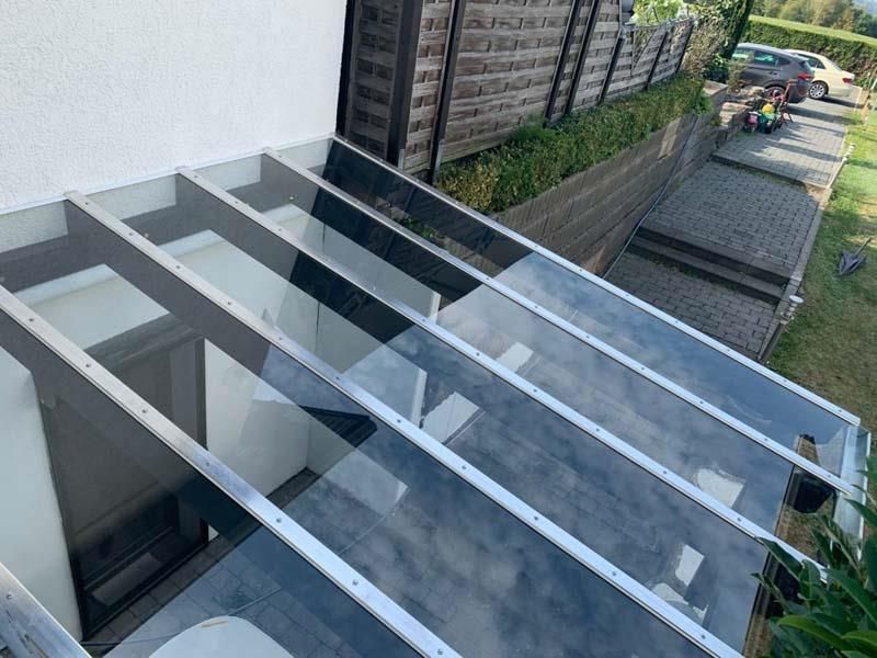 An der Seite eines Gebäudes wird ein Vordach mit einem Dach aus klarem Glas errichtet.