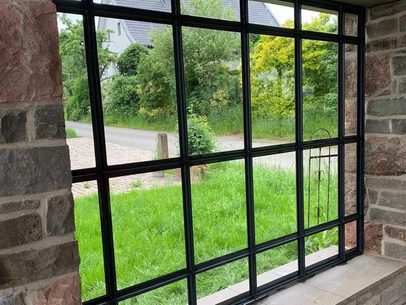 Ein großes Fenster in einer Steinmauer mit Blick auf eine Wiese.