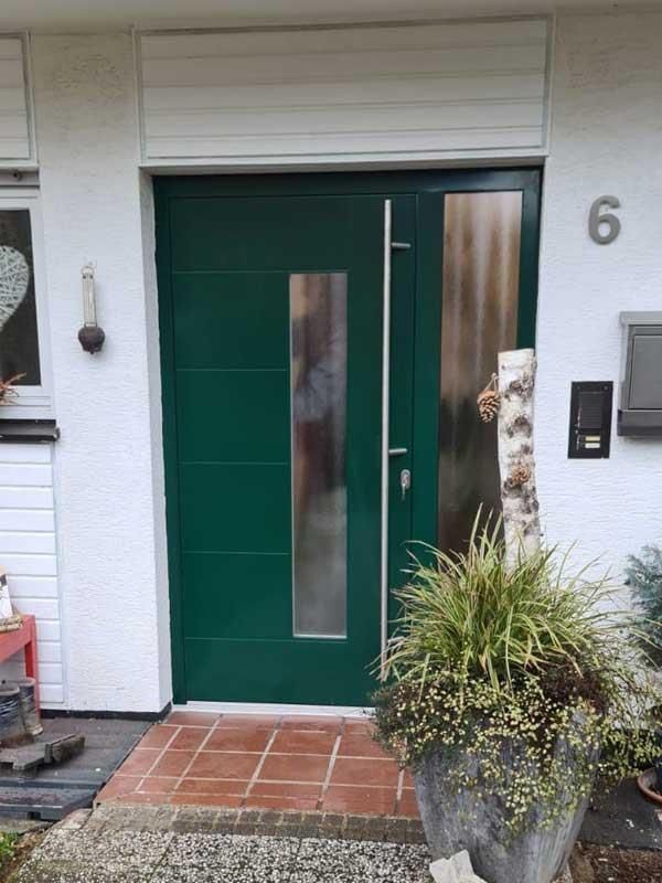 Die Haustür eines Hauses mit einer grünen Tür und einer Topfpflanze davor.