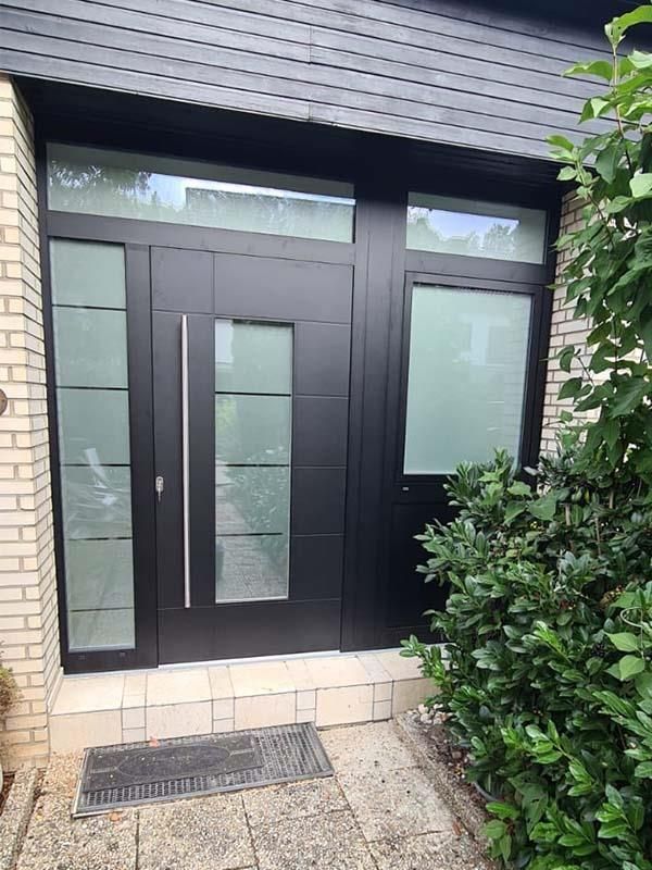 Vor einem Backsteingebäude befindet sich eine schwarze Tür mit einem Edelstahlgriff.