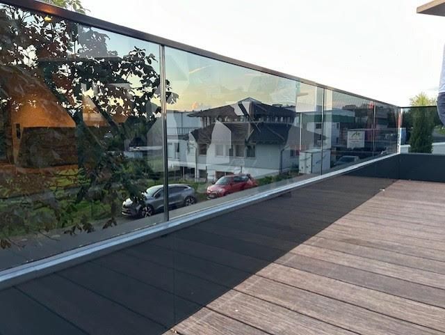 Eine Person steht auf einem Balkon mit Glasgeländer.