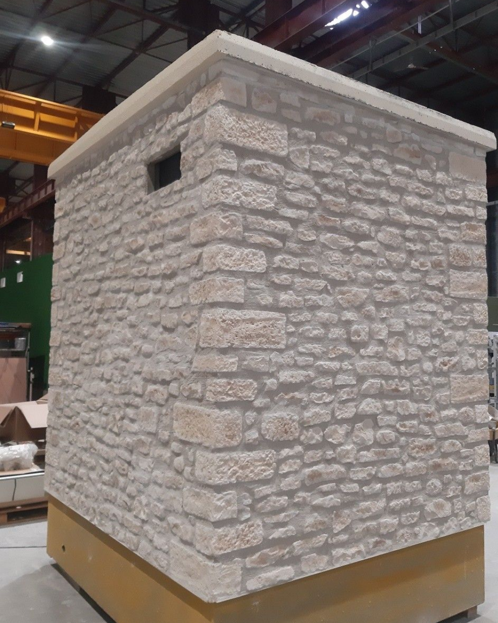 Structure carrée en pierre, percée d'une petite ouverture et surmontée d'une bordure en béton clair. Socle brun.