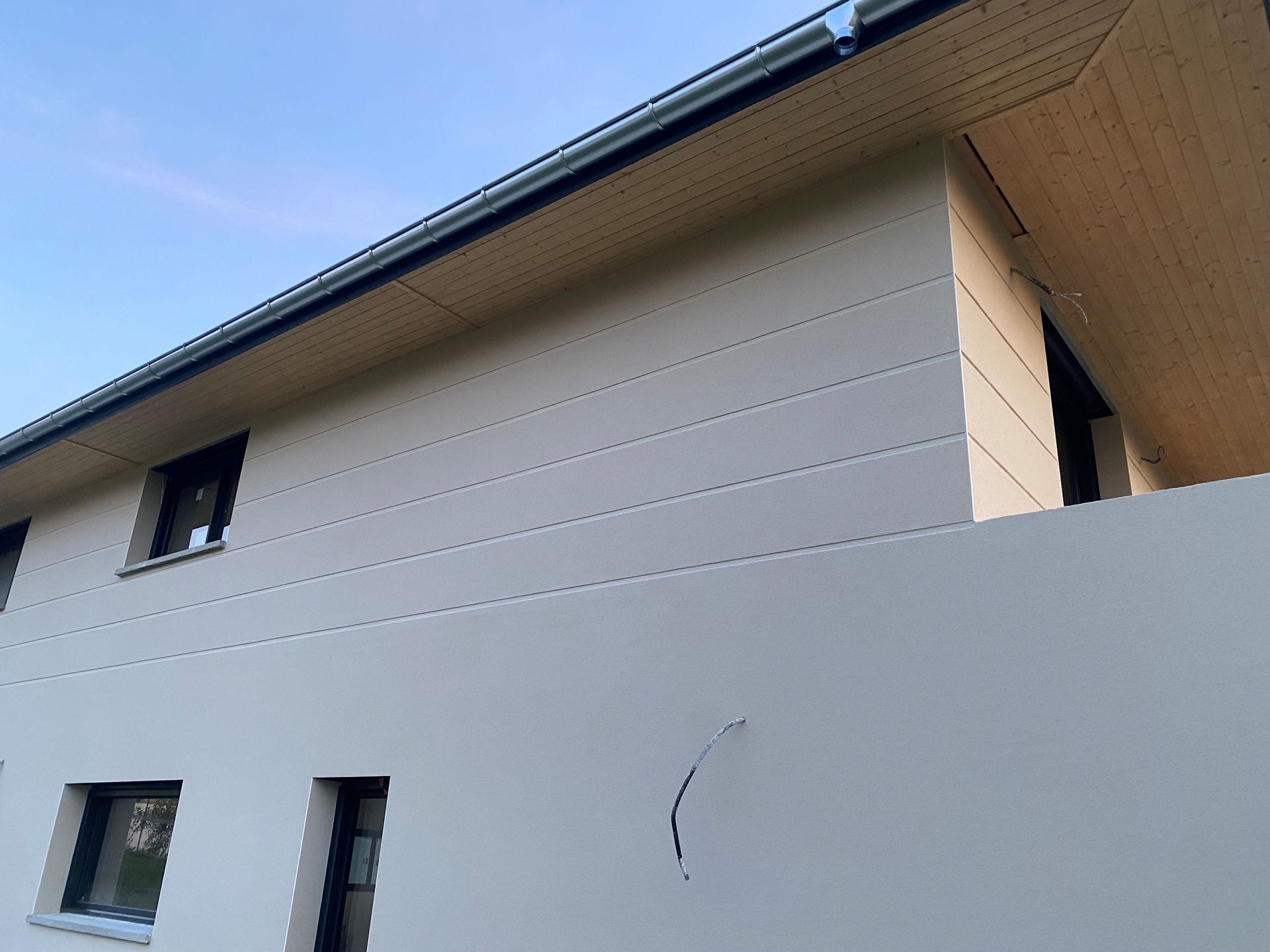 Bâtiment gris avec soubassement en pierre, petites fenêtres et toit en pente.