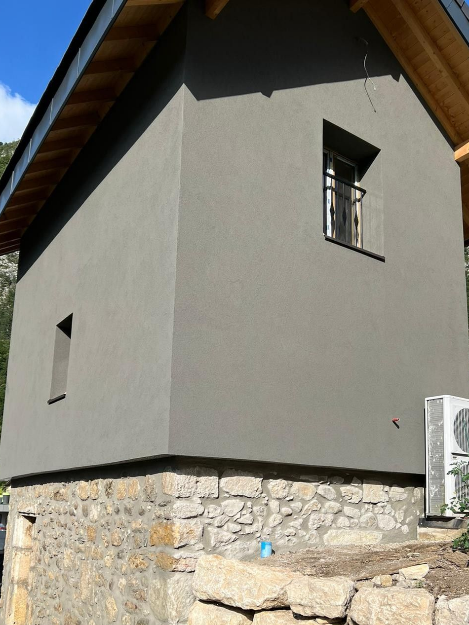 Bâtiment gris avec fondations en pierre, petites fenêtres et toit en bois.