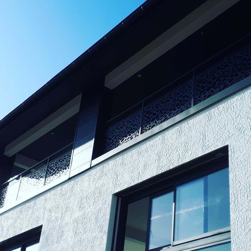 Vue extérieure d'un immeuble moderne gris avec des balustrades de balcon décoratives en métal, sous un ciel bleu dégagé.