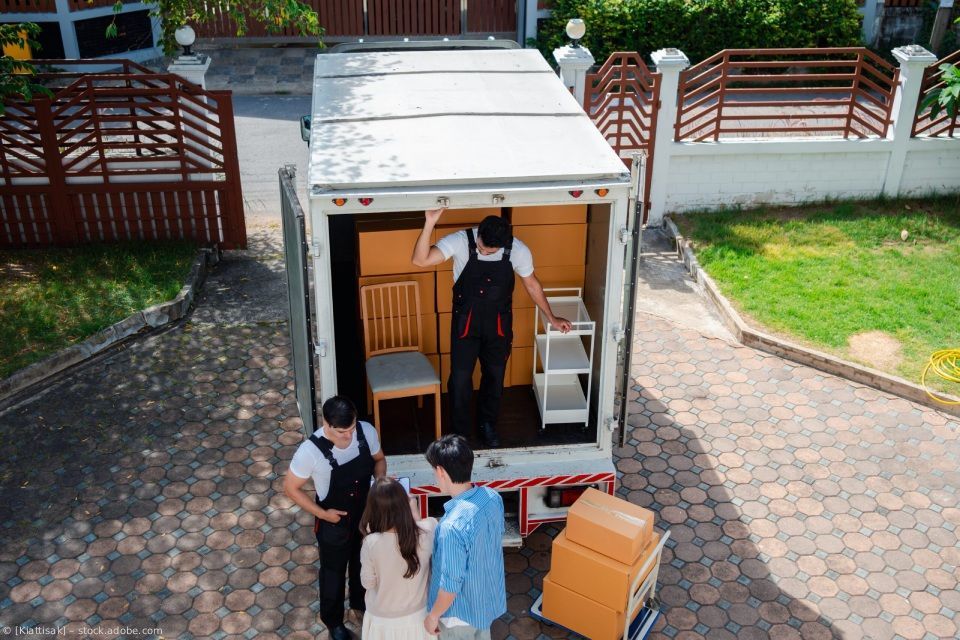 Menschen verladen Möbelkisten in einen weißen Lastwagen auf einer Einfahrt vor einem Haus