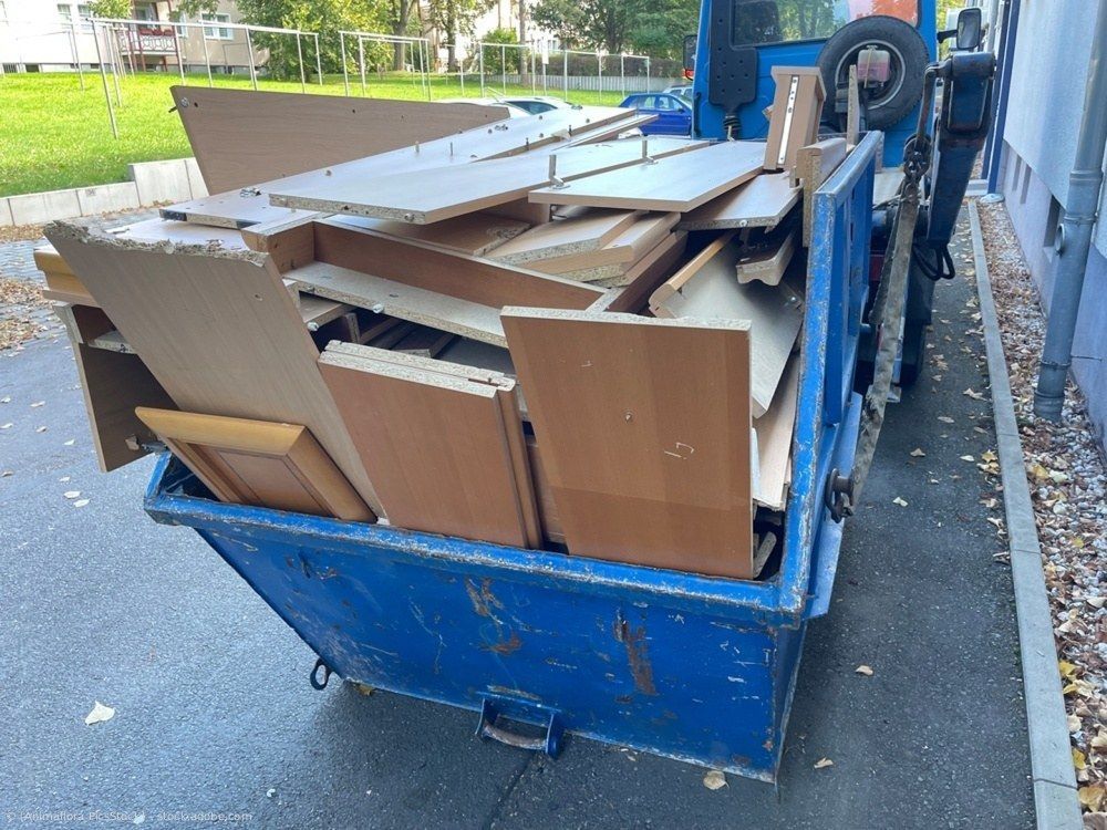 Ein blauer Müllcontainer voller Holz- und Pappbruch auf einer Straße