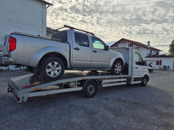 Dépanneuse transportant un pick-up argenté sur son plateau, dans un parking en gravier au crépuscule