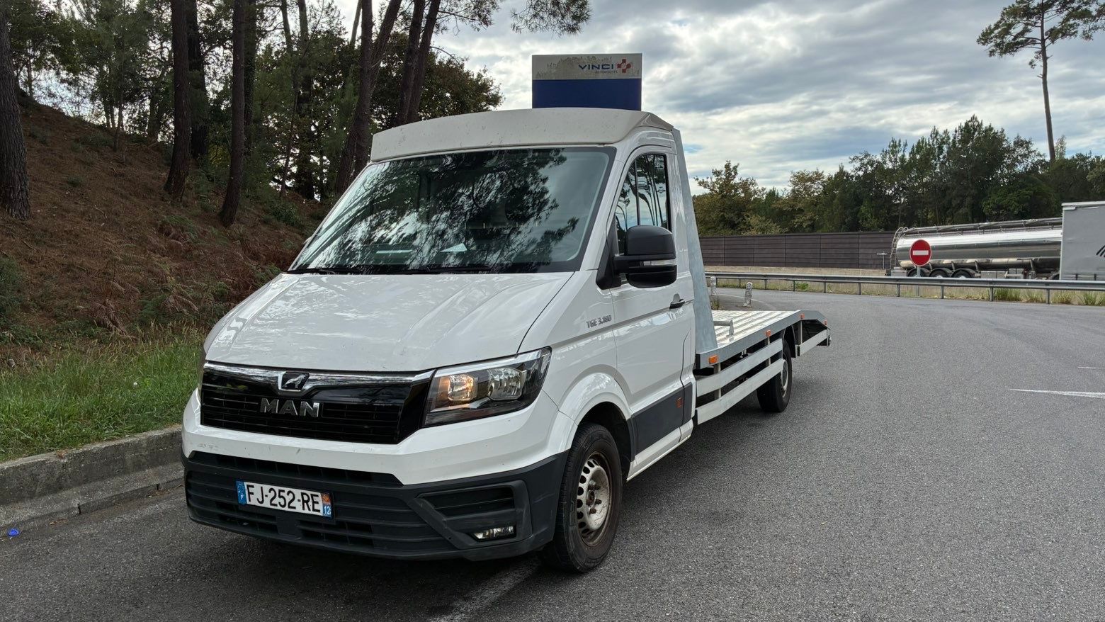 Camion plateau blanc garé sur le bord d’une route mouillée sous un ciel nuageux
